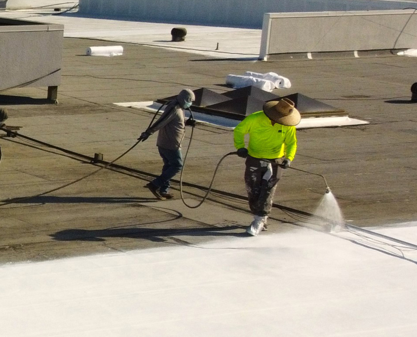 Two Workers Spraying Roof With Coating